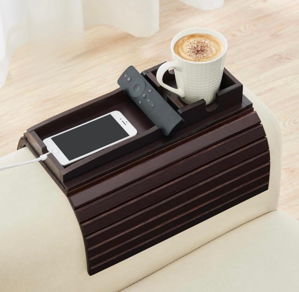Espresso bamboo sofa arm tray holding a coffee mug, remote and phone on a cream couch arm